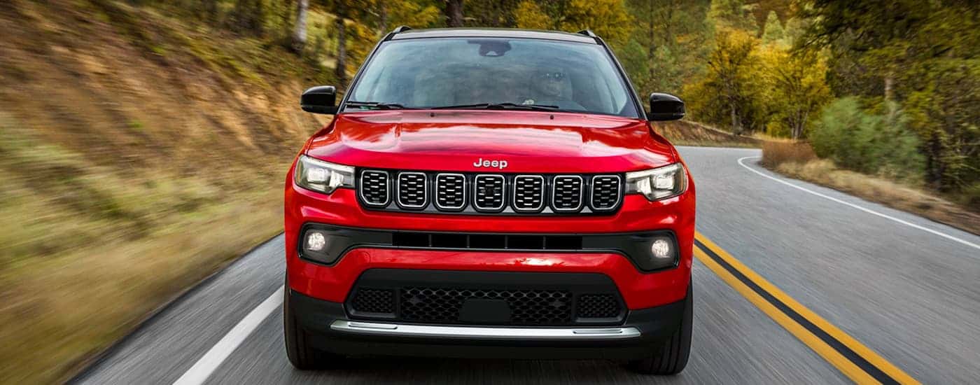 Red 2025 Jeep Compass driving down a rural road