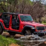 A red 2025 Jeep Wrangler Rubicon off-roading in water