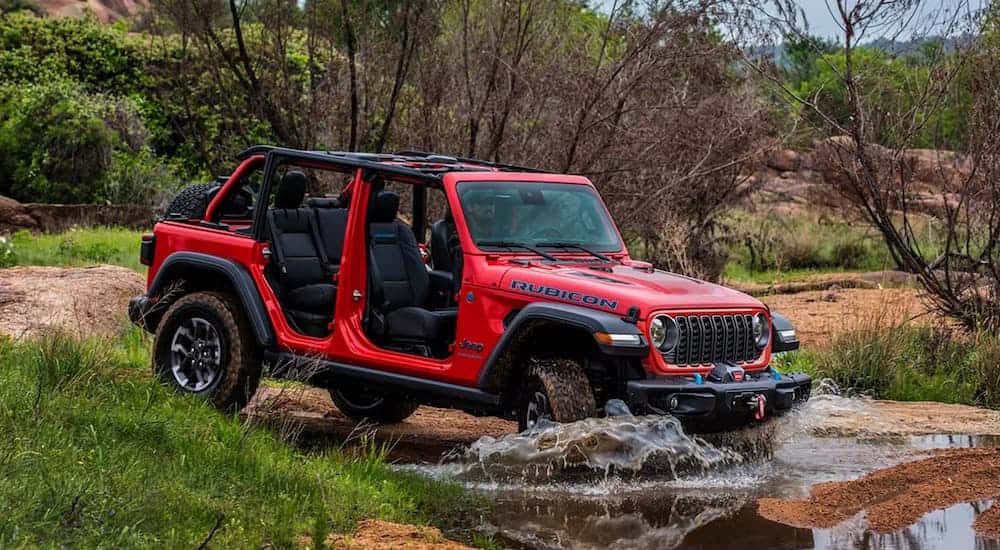 A red 2025 Jeep Wrangler Rubicon off-roading in water