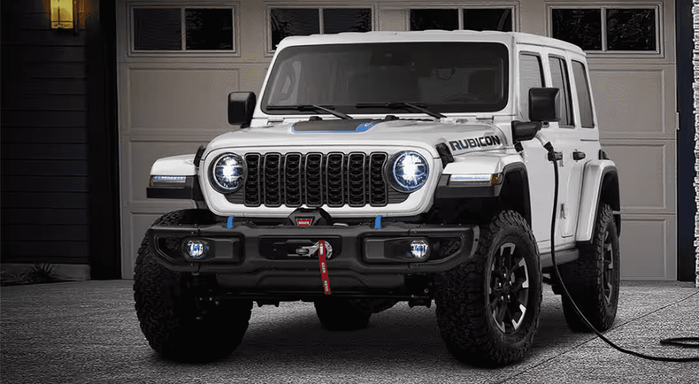 White 2025 Jeep Wrangler 4xe parked in front of a home charging. 