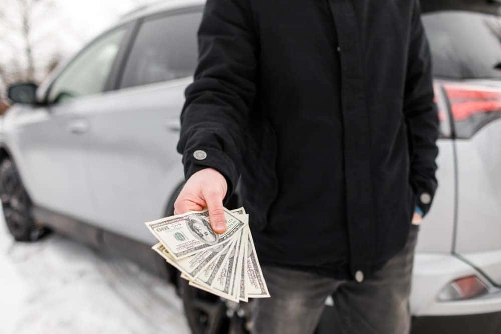Person standing in front of car while holding cash