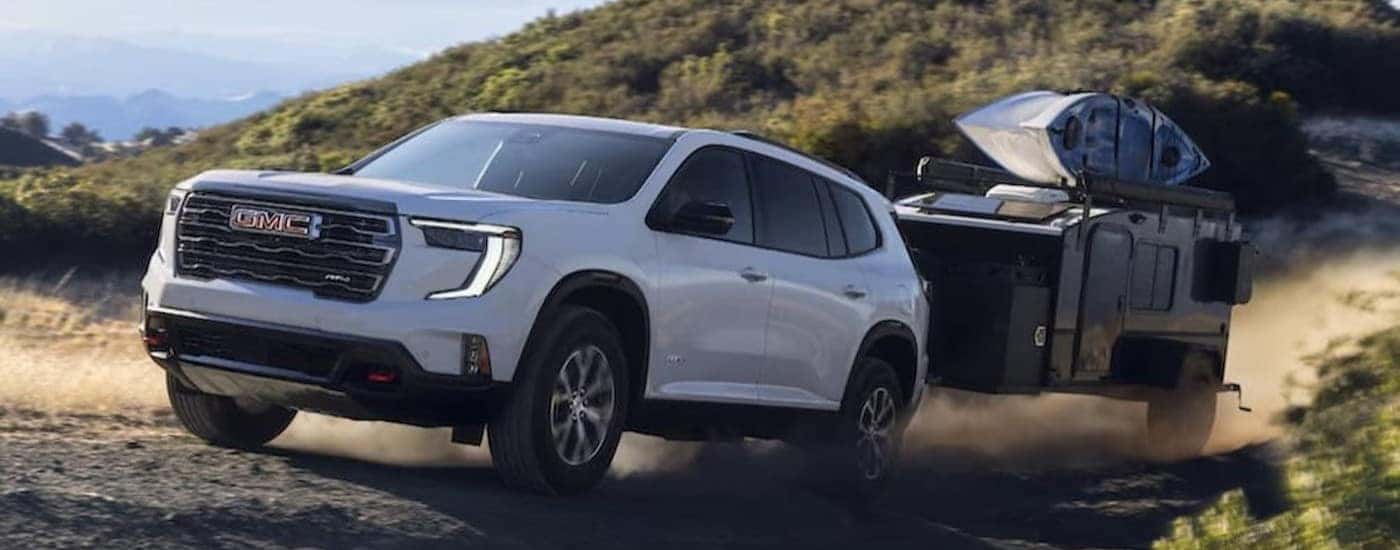 A white 2024 GMC Acadia AT4 is shown towing a trailer.