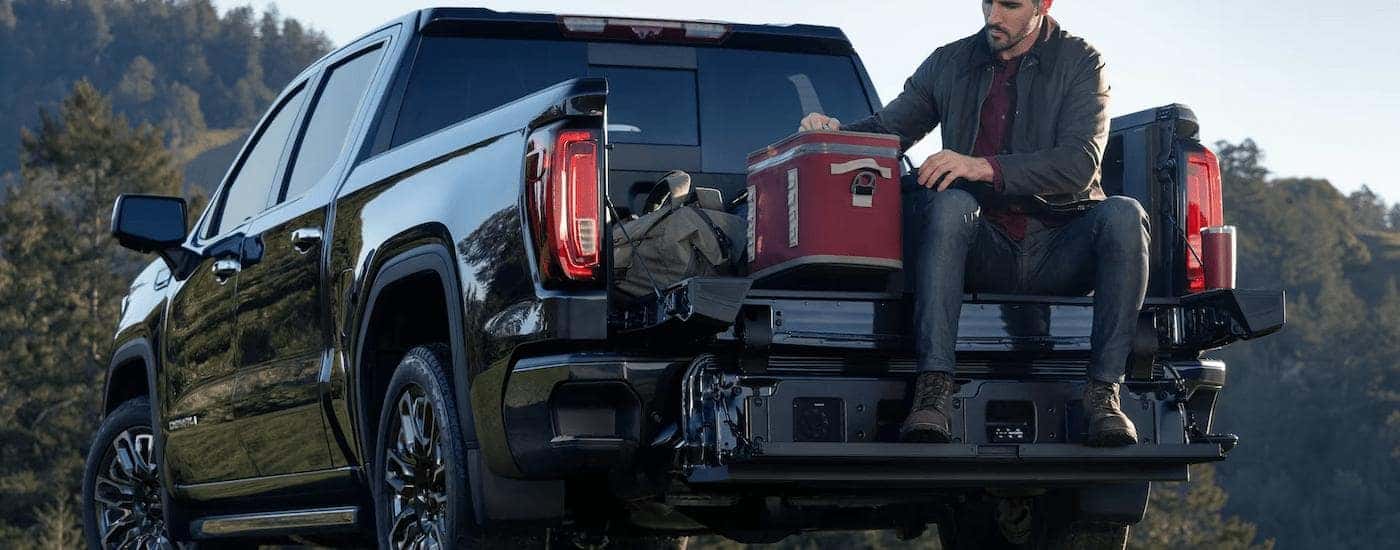 A man is sitting on the bed of a black 2023 GMC Sierra 1500 Denali.