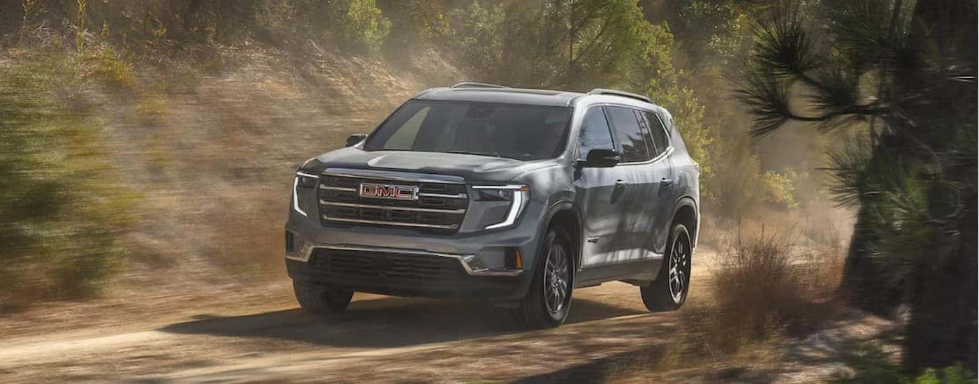 A silver 2025 GMC Acadia is shown driving on a dirt path.