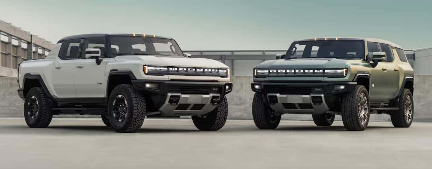 A white and a green 2025 GMC Hummer EV are facing each other.