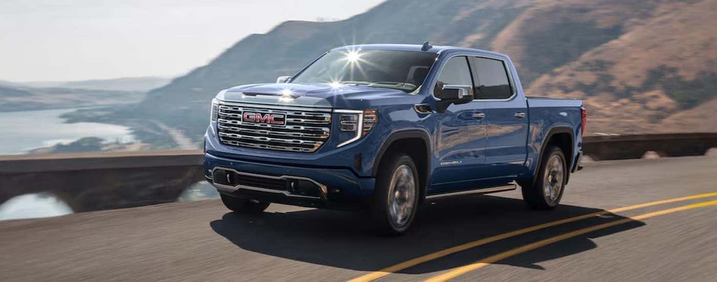 A blue 2025 GMC Sierra 1500 Denali driving on a highway.
