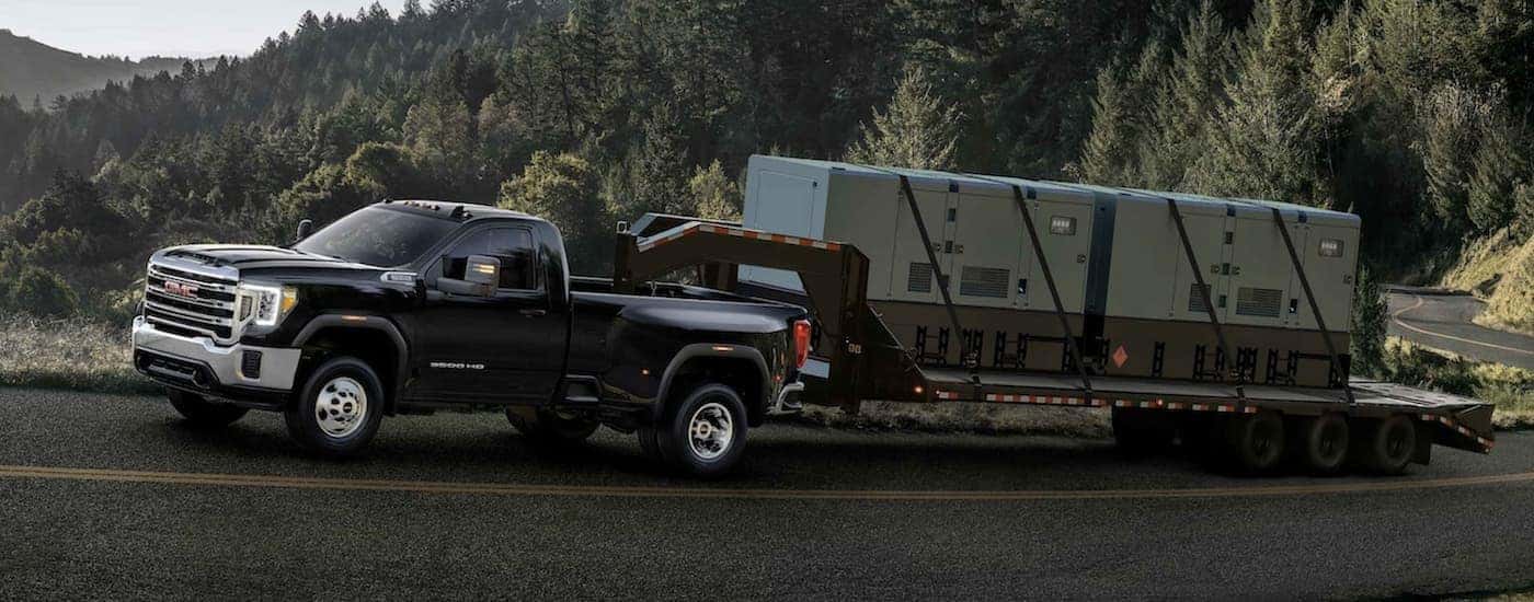 A black 2022 GMC Sierra 3500 towing a trailer on a highway.