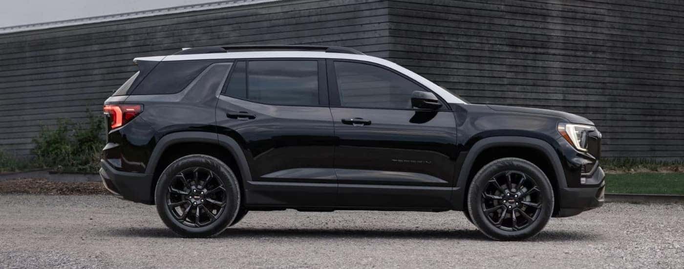 A black 2025 GMC Terrain for sale is shown parked near a wooden building.