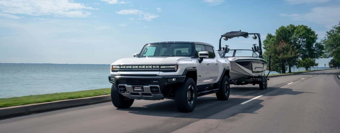 A white 2023 GMC Hummer EV towing a boat to a used car dealer.