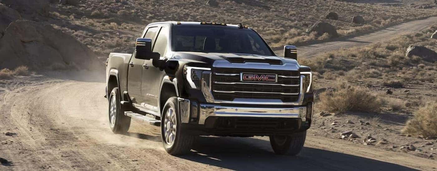 A black 2024 GMC Sierra 2500 HD driving on a dirt road.
