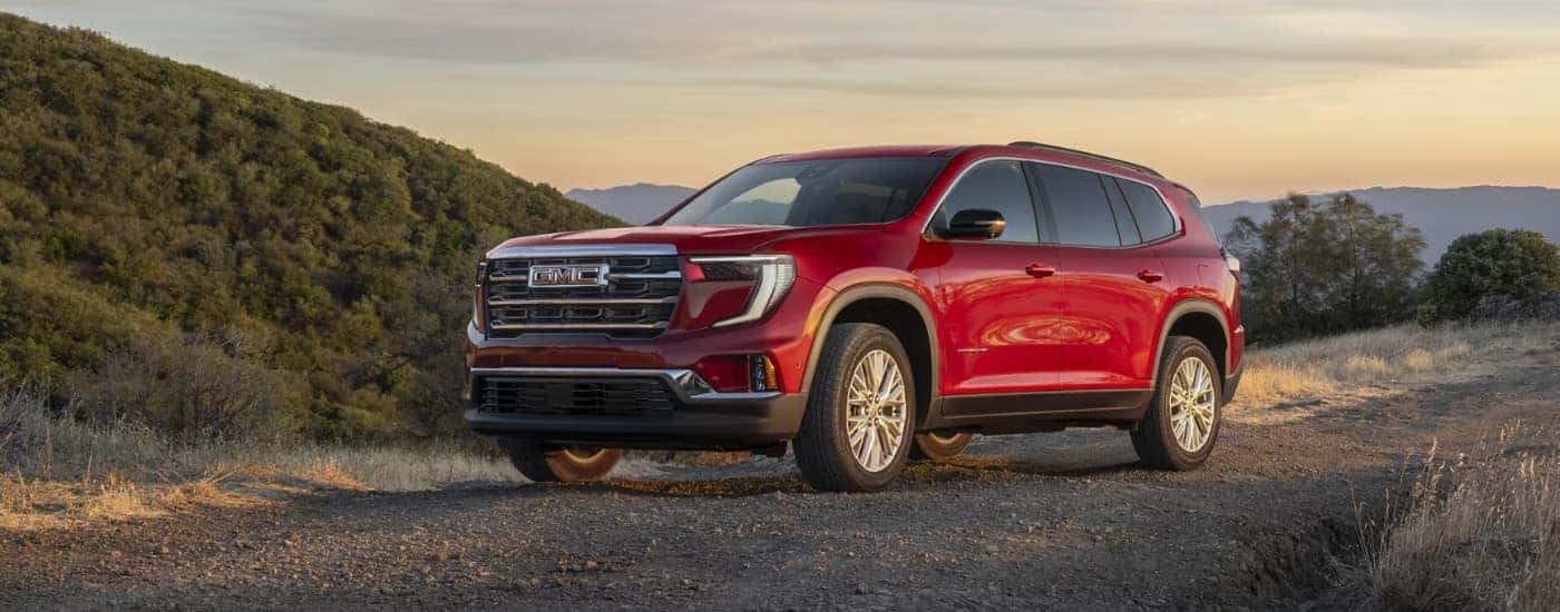 A red 2025 GMC Acadia parked off-road on a path