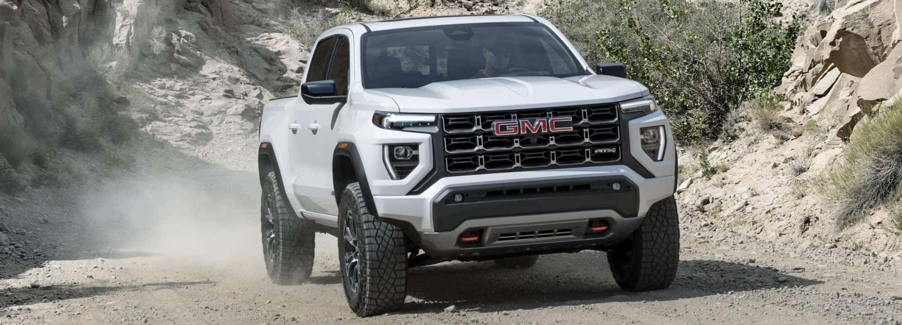 A white 2023 GMC Canyon driving on a gravel road.