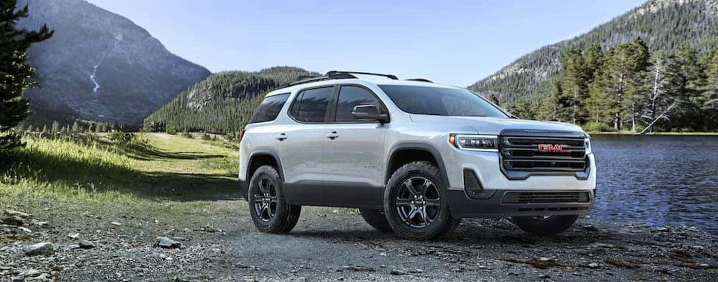 A white 2023 GMC Acadia AT4 is shown parked near a lake.