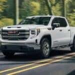 A white 2024 GMC Sierra 1500 SLE driving down a road