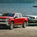 A red 2022 Chevy Silverado 1500 towing a boat out of a lake.