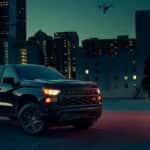 A black 2024 Chevy Silverado 1500 LT parked in a city parking lot at night.