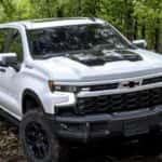 A white 2025 Chevy Silverado 1500 ZR2 Bison parked off-road in a forest.