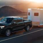 A black 2024 Chevy Silverado 1500 High Country towing a trailer on the highway.