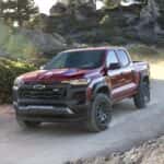 A red 2024 Chevy Colorado Trail Boss drives around a dirt bend.