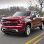 A red 2019 Chevy Silverado 1500 RST driving by a lake from a dealer with used trucks for sale near Jersey Village.