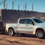 A white 2023 Chevy Silverado 1500 WT towing heavy equipment at a construction site.