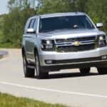 A popular used Chevy Tahoe for sale, a silver 2015 Chevy Tahoe LT, is shown driving on a highway.