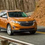 An orange 2019 Chevy Equinox is shown from the front at an angle after leaving a dealer that has used SUVs for sale.
