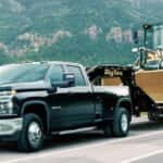 A black 2020 Chevy Silverado 3500 HD is shown from the front at an angle while towing a loader after leaving a dealer that has used trucks for sale near Spring, TX.