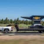 A white 2020 Chevy Silverado 3500 HD is shown from the side while towing a giant anvil.