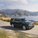 A green 2023 Chevy Tahoe High Country is shown from the side on a coastal road.