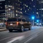 A brown 2024 Chevy Tahoe RST is shown from the rear at an angle while driving through the city after leaving a dealer that has a Chevy Tahoe for sale.