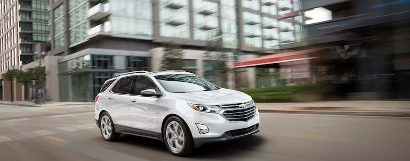 A white 2019 Chevy Equinox is shown driving on a city street after leaving a Aldine used Chevy dealer