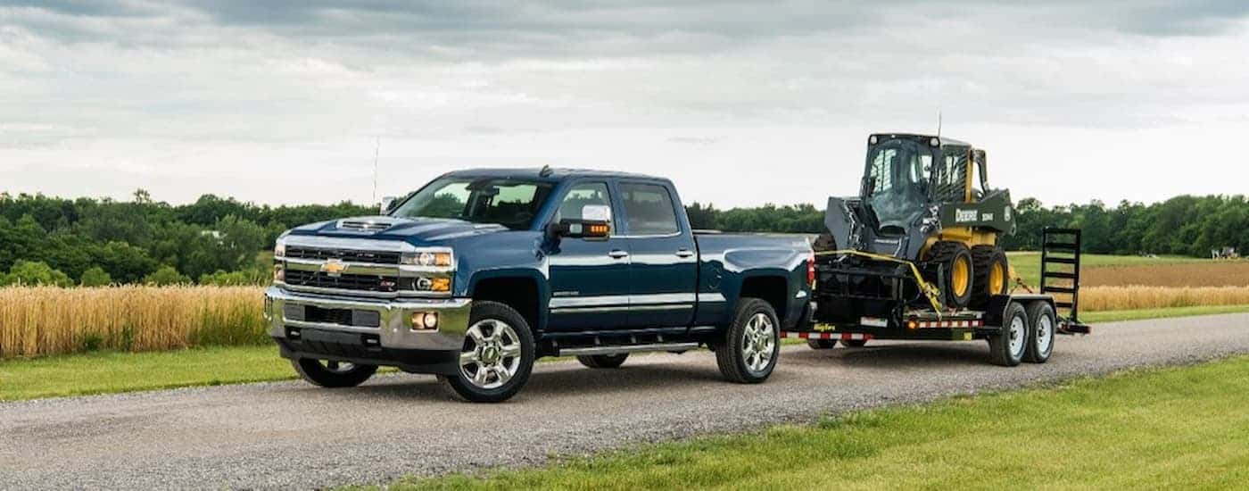 A blue 2019 Chevy Silverado 2500HD is shown towing heavy machinery after leaving a certified pre-owned Silverado dealer