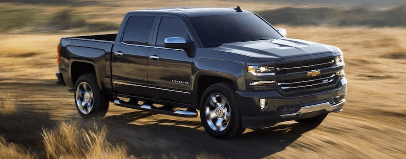 A black 2018 certified pre-owned Chevy Silverado 1500 is shown driving through a dry grassy field