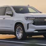A white 2023 Chevy Tahoe is shown from the side driving on an open road.