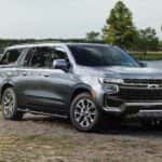 A grey 2021 Chevy Suburban Z71 is shown parked in front of a lake.