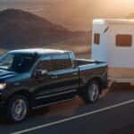 A black 2022 Chevy Silverado 1500 is shown from the side towing a white closed trailer on an open road.