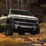 A tan 2024 Chevy Silverado EV Trail Boss is shown parked in the woods after visiting a Houston electric Silverado dealer.