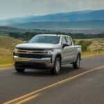 A silver 2020 Chevy Silverado LT is driving on a highway in front of mountains.