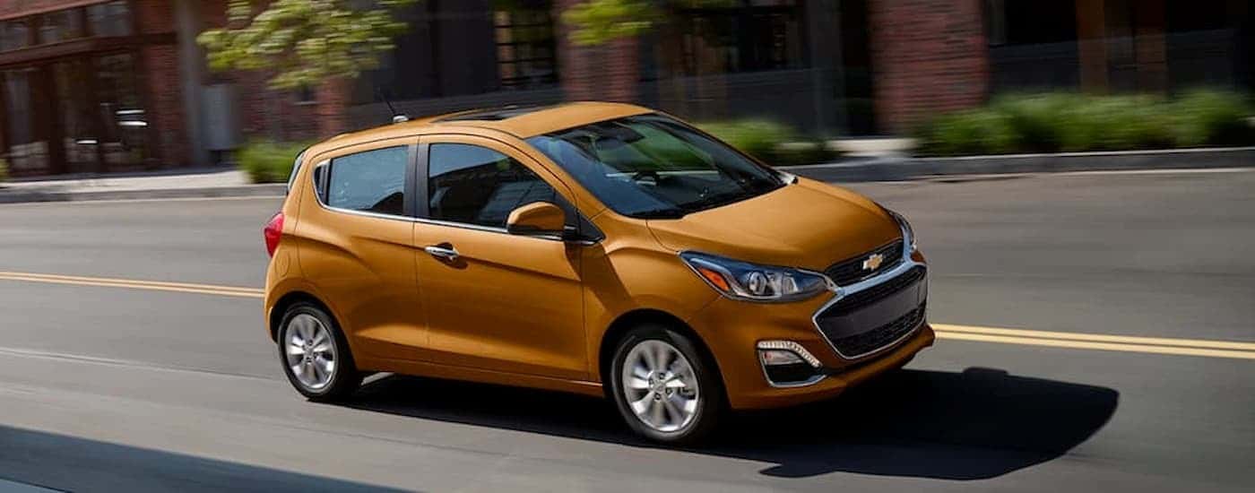 An orange 2020 Chevy Spark is shown from the side driving on a city street