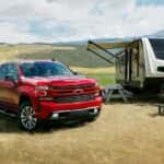 A red 2022 Chevy Silverado 1500 RST LTD is shown parked next to a camper in a field.