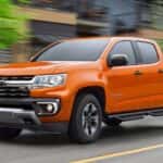 A orange 2021 Chevy Colorado is driving through a city.