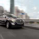 A grey 2016 used Chevy Equinox is shown driving past a blurred city.