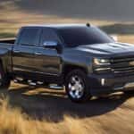 A black 2018 used Chevy Silverado is driving on a dirt road past a field.