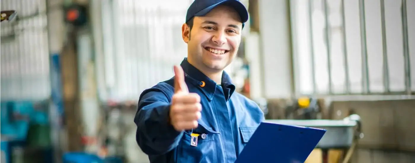 A mechanic is shown standing in a repair shop giving a thumbs up.