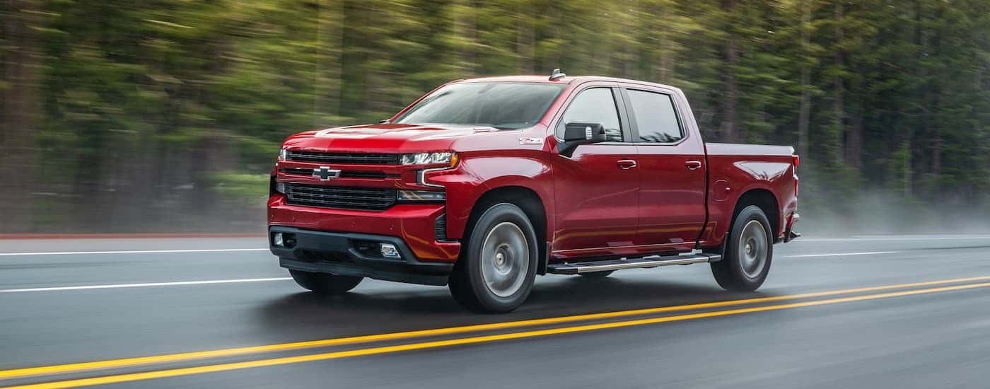 A red 2020 Chevy Silverado 1500 is shown driving on a tree-lined road