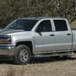 A grey 2018 Chevy Silverado 1500 is shown from the side parked in a tree-lined field.