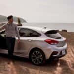 A white 2019 Chevy Cruze is shown parked on a beach at sunset.