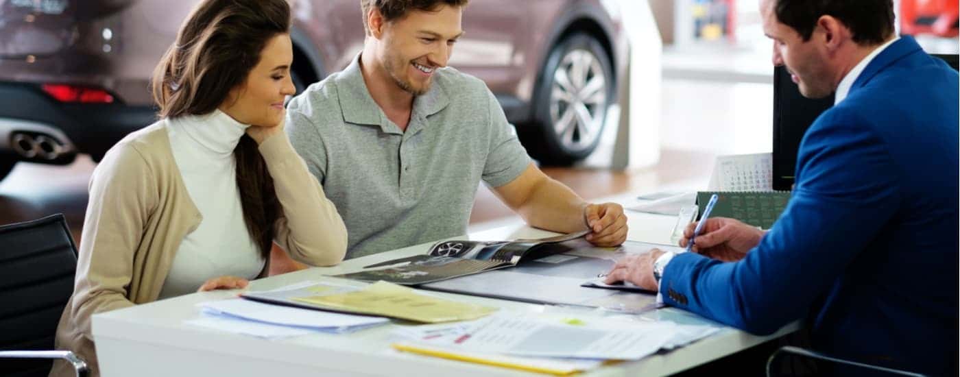 A car salesman is shown speaking to a couple about financing paperwork