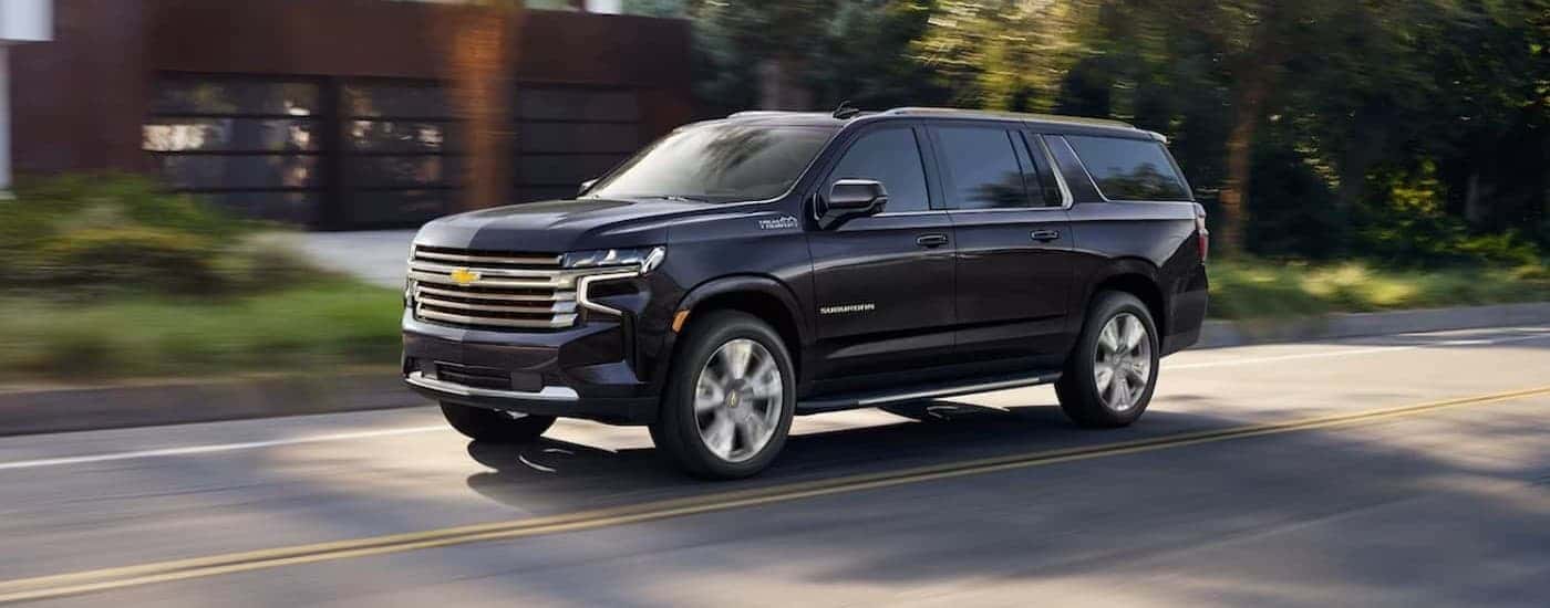 A blue 2023 Chevy Suburban High Country driving on a city street.